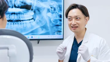 明るい笑顔で、患者さんと丁寧な診察を行う歯科医師。