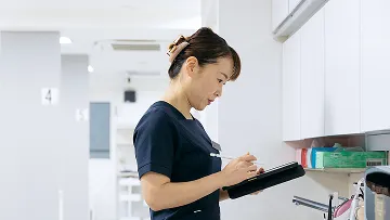 明るい病院の廊下で、真剣な表情でタブレット端末を操作する医療従事者。