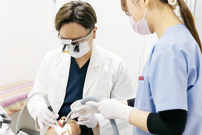 歯科医とアシスタントが連携して患者の口腔内治療を行っている様子。拡大鏡を装着している。