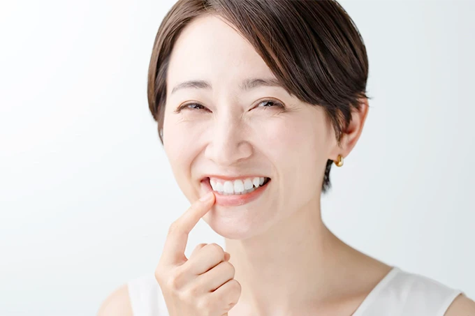 笑顔で歯を見せながら前歯を指さしている女性。白い背景とノースリーブの服装が爽やかな印象を与える。