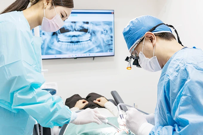 歯科医師が手術用手袋を着用し、口腔外科手術を行っている様子。手術器具と吸引器が使用されている。