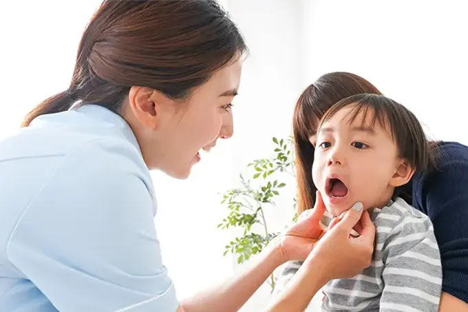 歯科衛生士が小さな男の子の口の中を優しく診察している様子。保護者が隣で見守っている。
