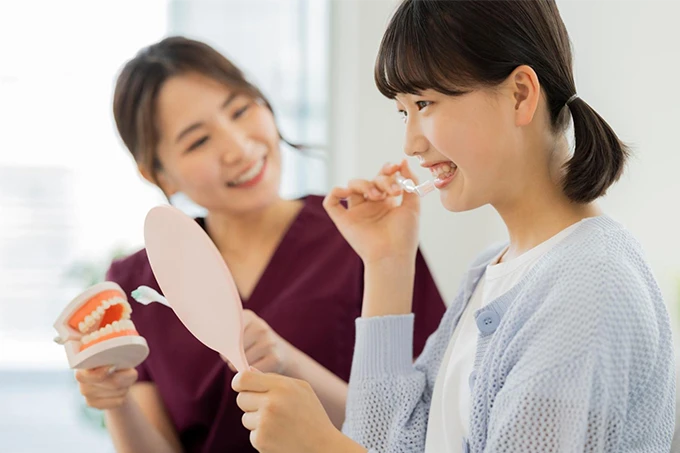 歯科衛生士が女の子に模型と鏡を使って歯磨き指導をしている様子。