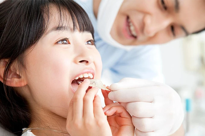 歯科医師のサポートのもと、女の子が矯正装置を口に装着しようとしている様子。
