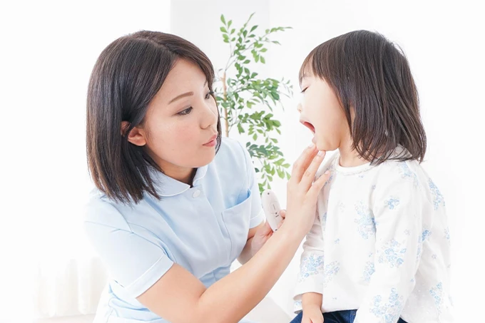 歯科スタッフが小さな女の子の口腔内をやさしくチェックしている様子。子どもは口を開けて診察に応じている。