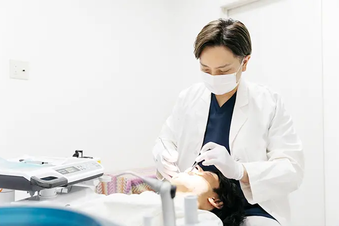 歯科医師が診療チェアの患者に対してマスクと手袋を着用して歯科治療を行っている様子。